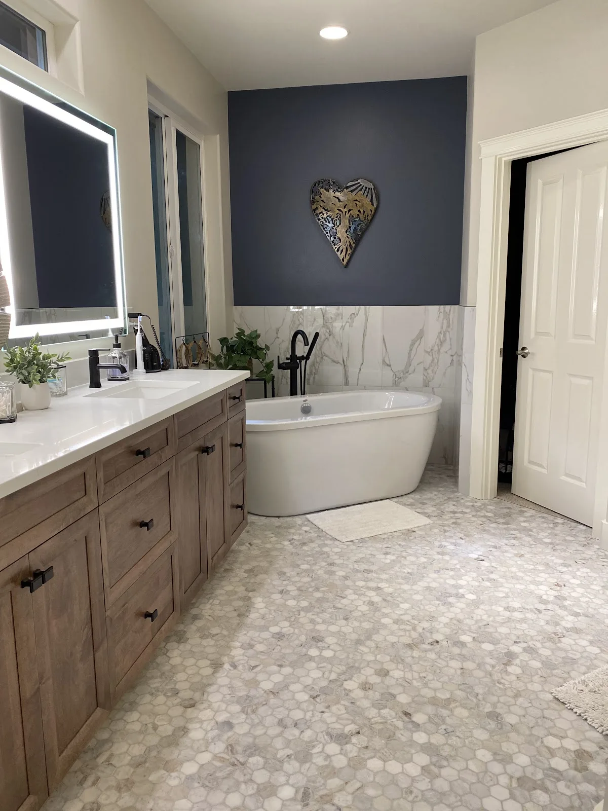 Blaine primary bathroom with navy wall, marble-look tile, wood vanity and freestanding tub in Blaine, WA — Living By Design