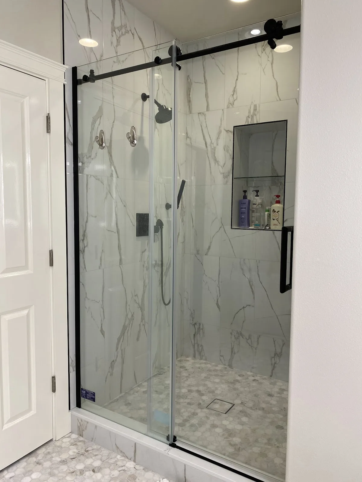 Blaine primary bathroom with navy wall, marble-look tile, wood vanity and freestanding tub in Blaine, WA — Living By Design (2)